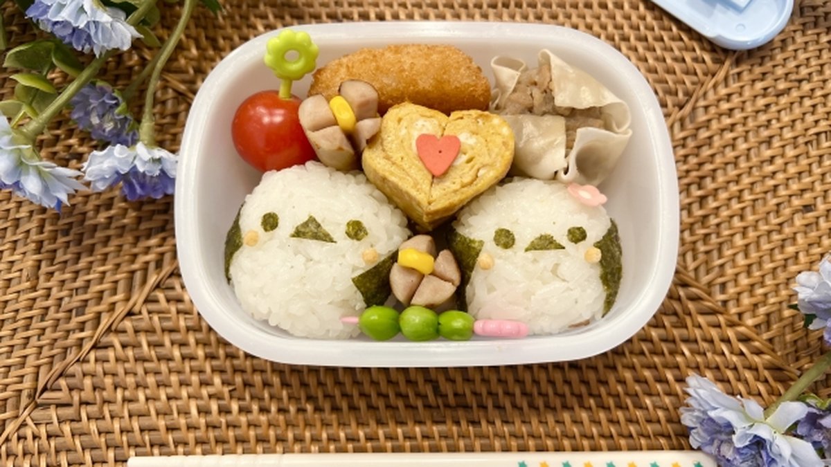 Two bird-shaped character onigiri (キャラ弁) in a white bento box with edamame, tamagoyaki, and gyoza — a typical example of Japanese character bento